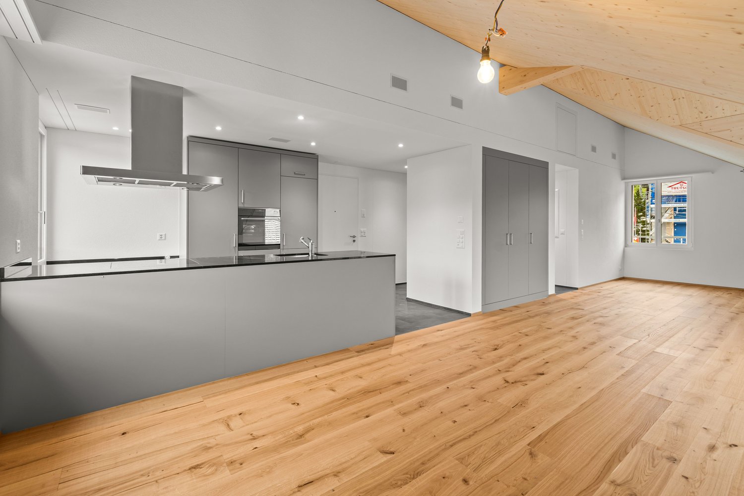 Open concept kitchen with hardwood floor, modern cabinets, ceiling exhaust, white walls, small window, hanging light