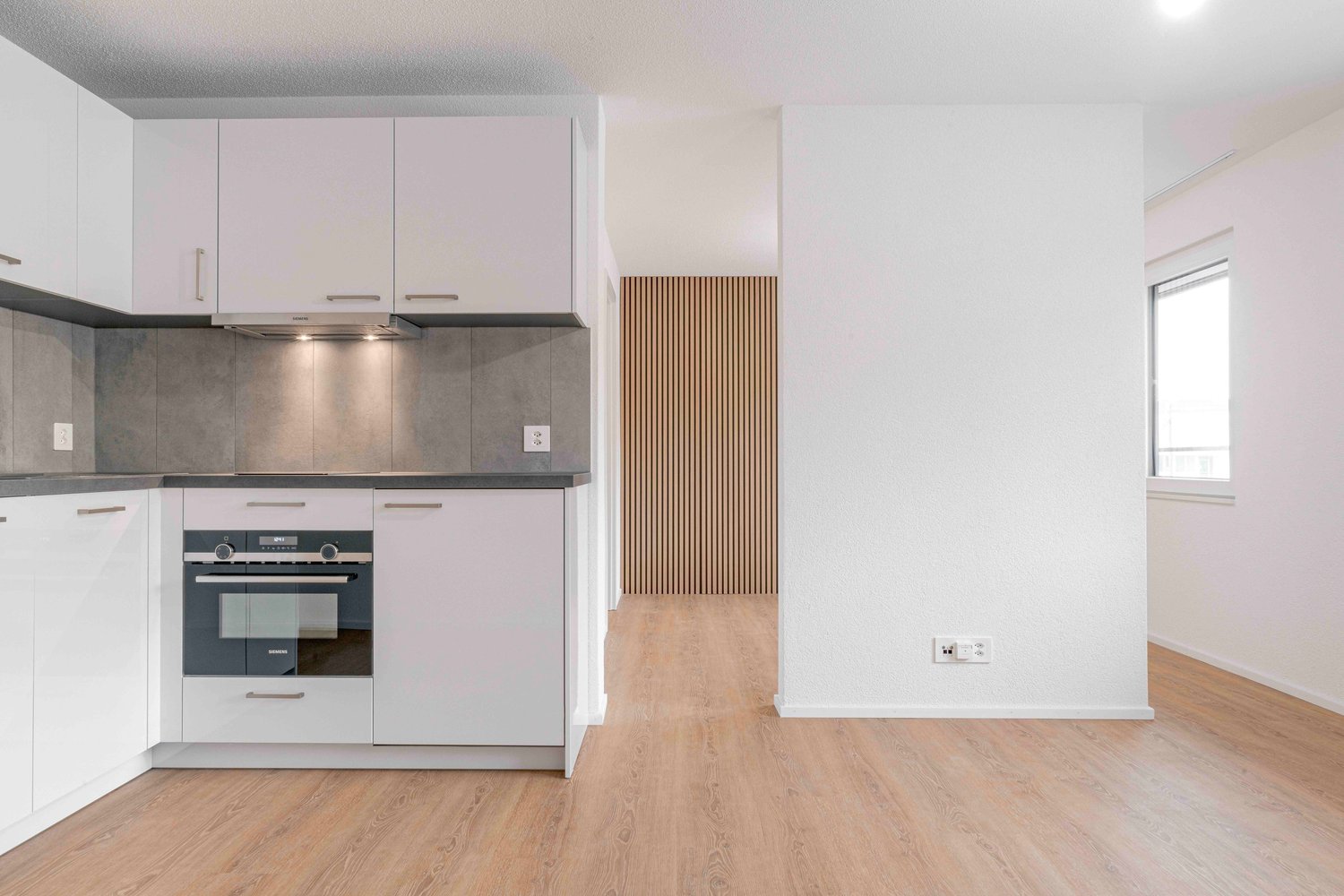 modern kitchen with white cabinets, wooden floor, built-in oven, extractor hood, power outlets, and a window