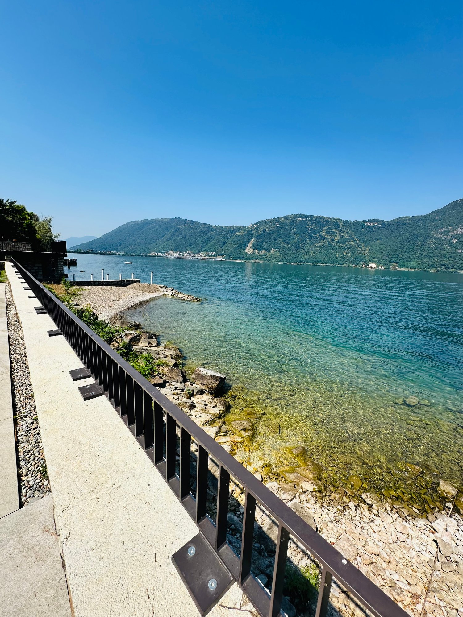 Pathway with railings, rocky shore, clear water, mountains in the distance