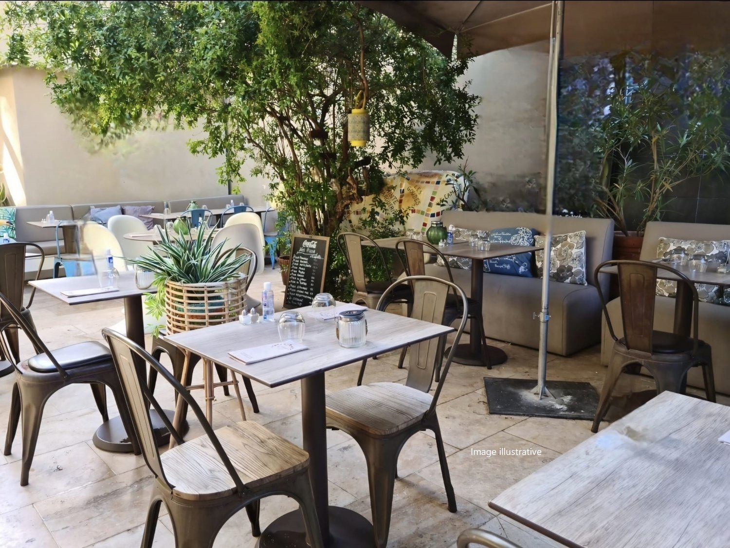 Outdoor seating area with tables, chairs, umbrellas, plants, and a chalkboard menu.