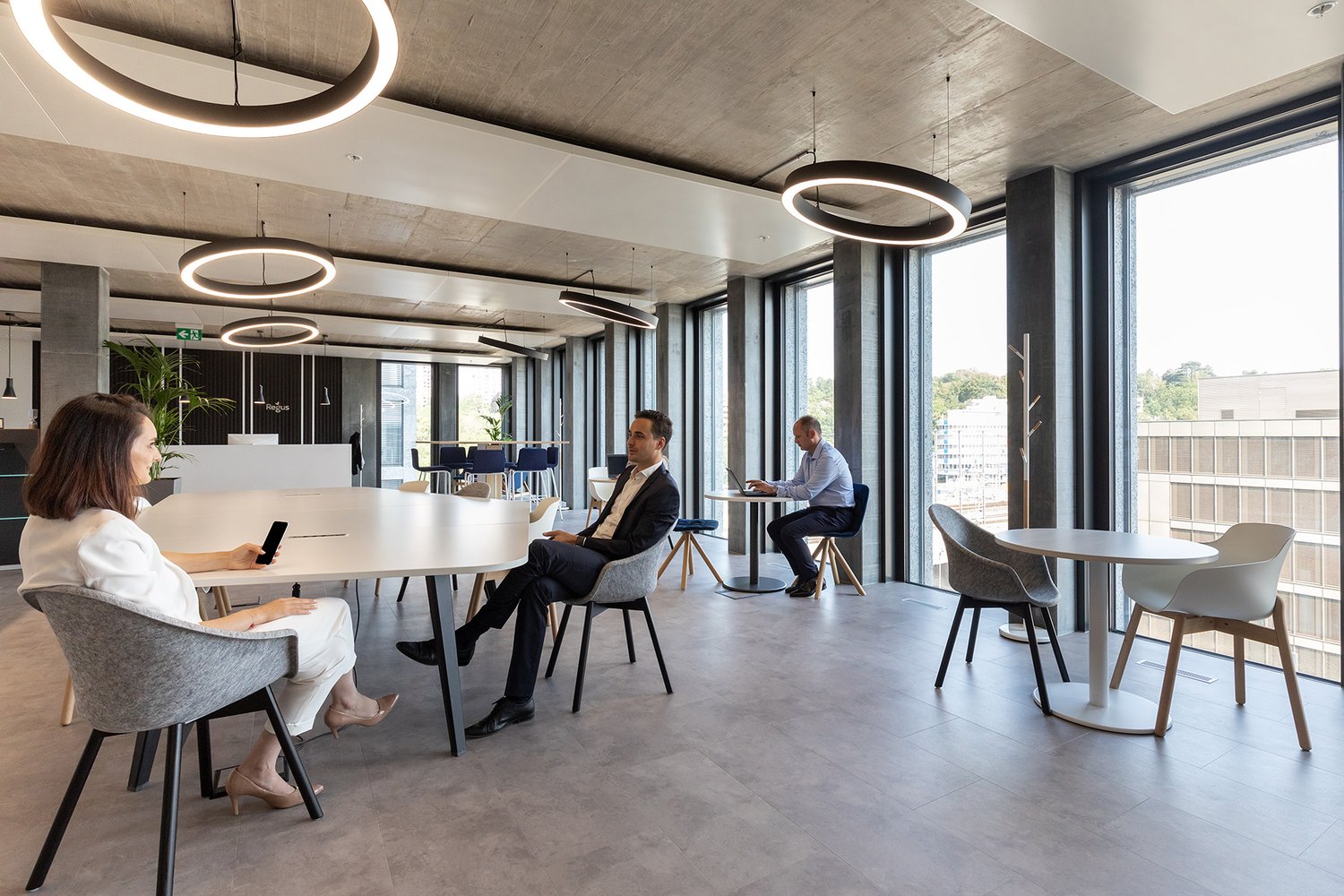 modern office space with large windows, circular lights, round tables, chairs, and people working