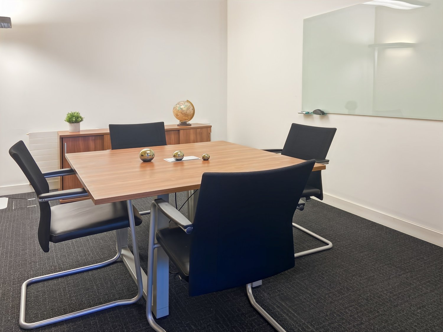 Spacious office with a wooden conference table, black leather chairs, a sideboard, and a mirror on the wall. The room has a modern and minimalist design with a clean and organized layout.
