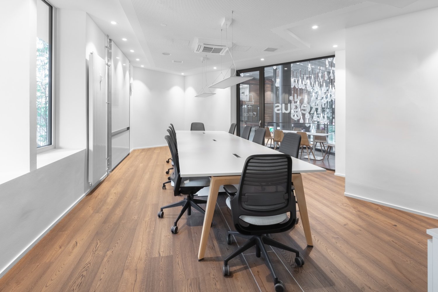 modern office room, long white desk, black chairs, white walls, wooden floor, natural light from windows