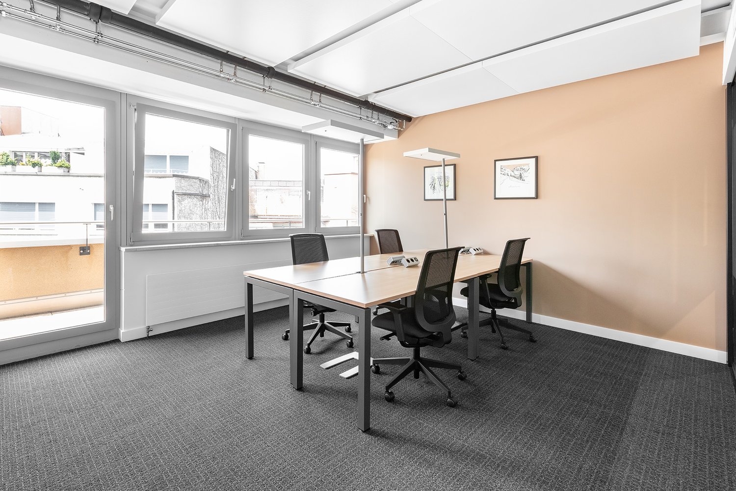 empty office room with desk, 6 chairs, tables, white walls, carpeted floor, large windows, picture frames