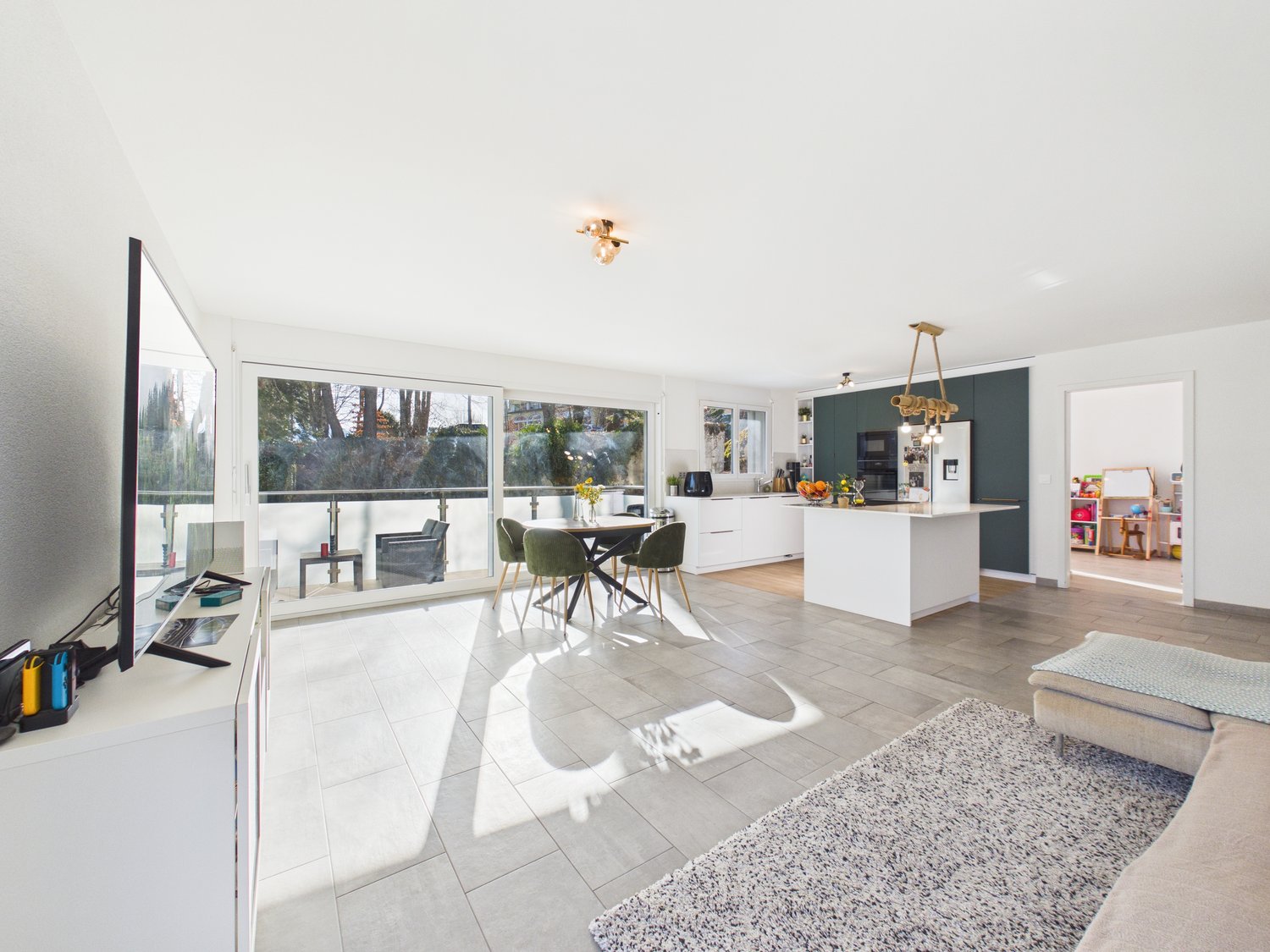 living area with white walls, white tile flooring, dining table with chairs, couch, television, kitchen island, chandelier, large windows
