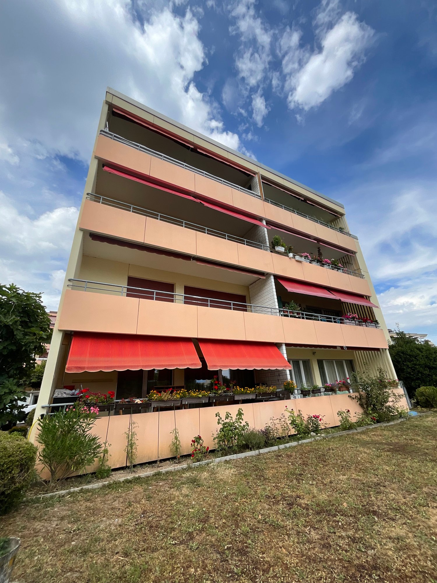 4 story apartment building, beige walls, red awnings, balconies with plants
