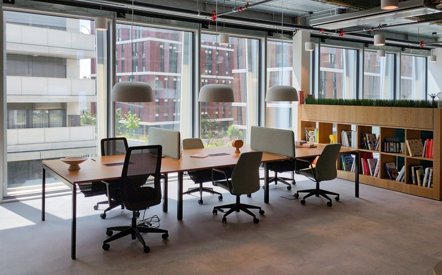 Modern office space with large windows overlooking the city, wooden conference table, black office chairs, bookshelves, and potted plants