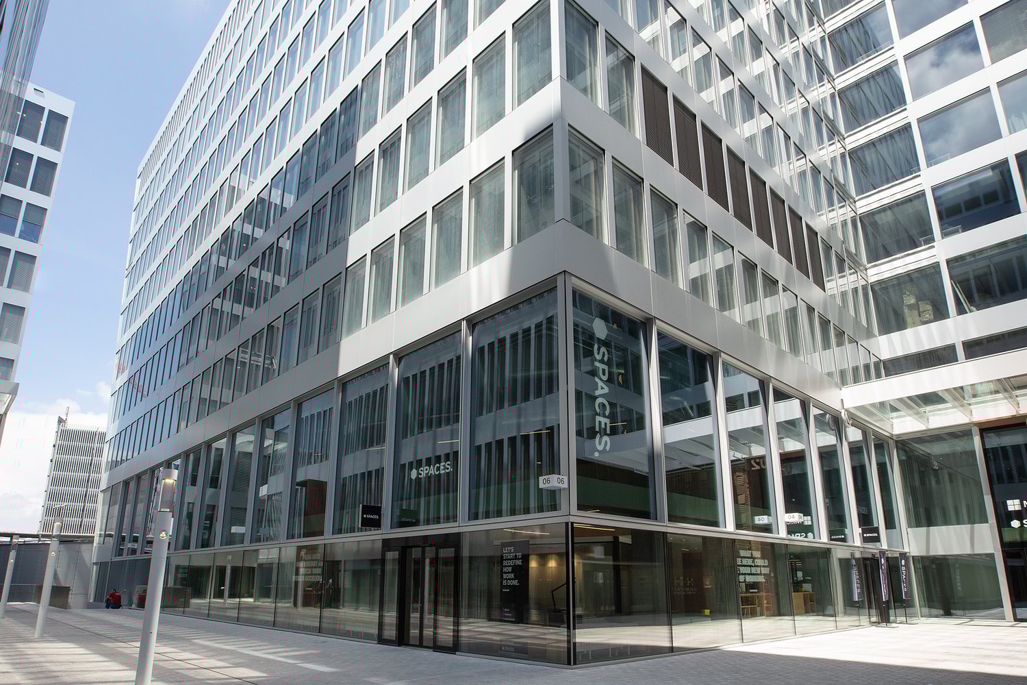 Multi-story glass and steel commercial building with a ground floor entrance and signage for 'Spaces', indicating it is likely an office or co-working space.