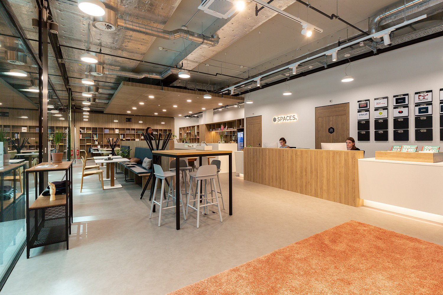 modern office space with glass walls, long desk, and reception area with wooden countertops, people working, shelves, and furniture