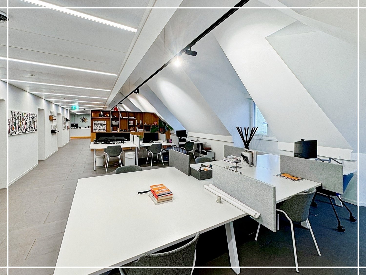 modern office space with white walls, white desks, gray chairs, bookshelves, monitors, and ceiling lights