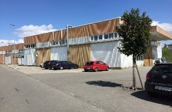 Industrial building with multiple windows, cars parked in front, tree in front