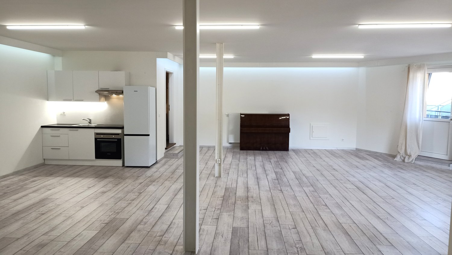 Empty room with wooden floor, white kitchen, fridge, oven, sink, wooden storage unit