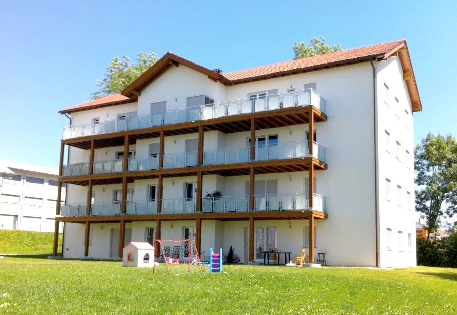 White apartment building with multiple balconies, red roof, large grassy area in front