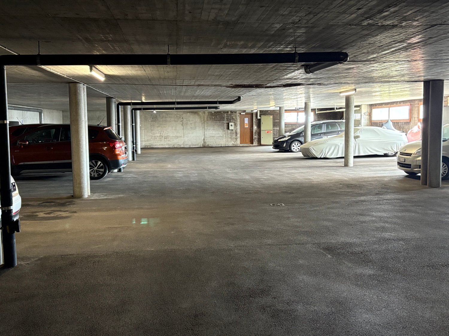 Indoor parking garage with concrete floor, concrete ceiling, and several parked cars