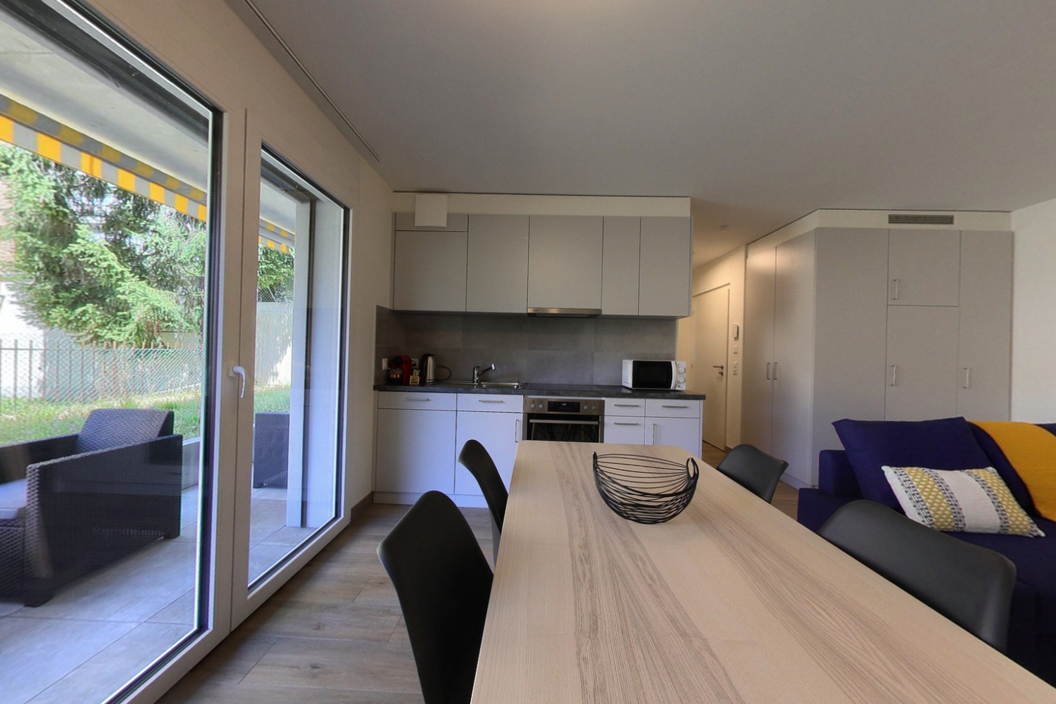 modern kitchen with dining area, large windows, wooden floor, white cabinets, modern appliances, dining table, chairs, couch with pillows