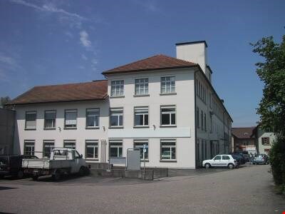 white building, brown roof, multiple windows, parking lot, cars parked