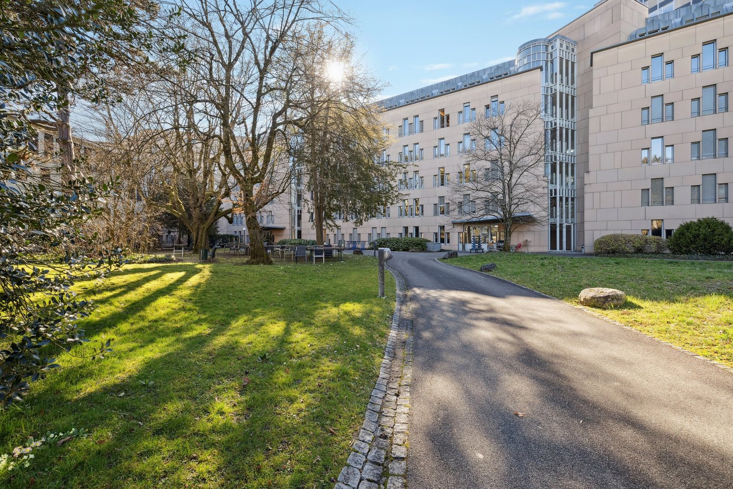 Large modern building with multiple windows and two glass doors. Green grass lawn. A wide driveway.