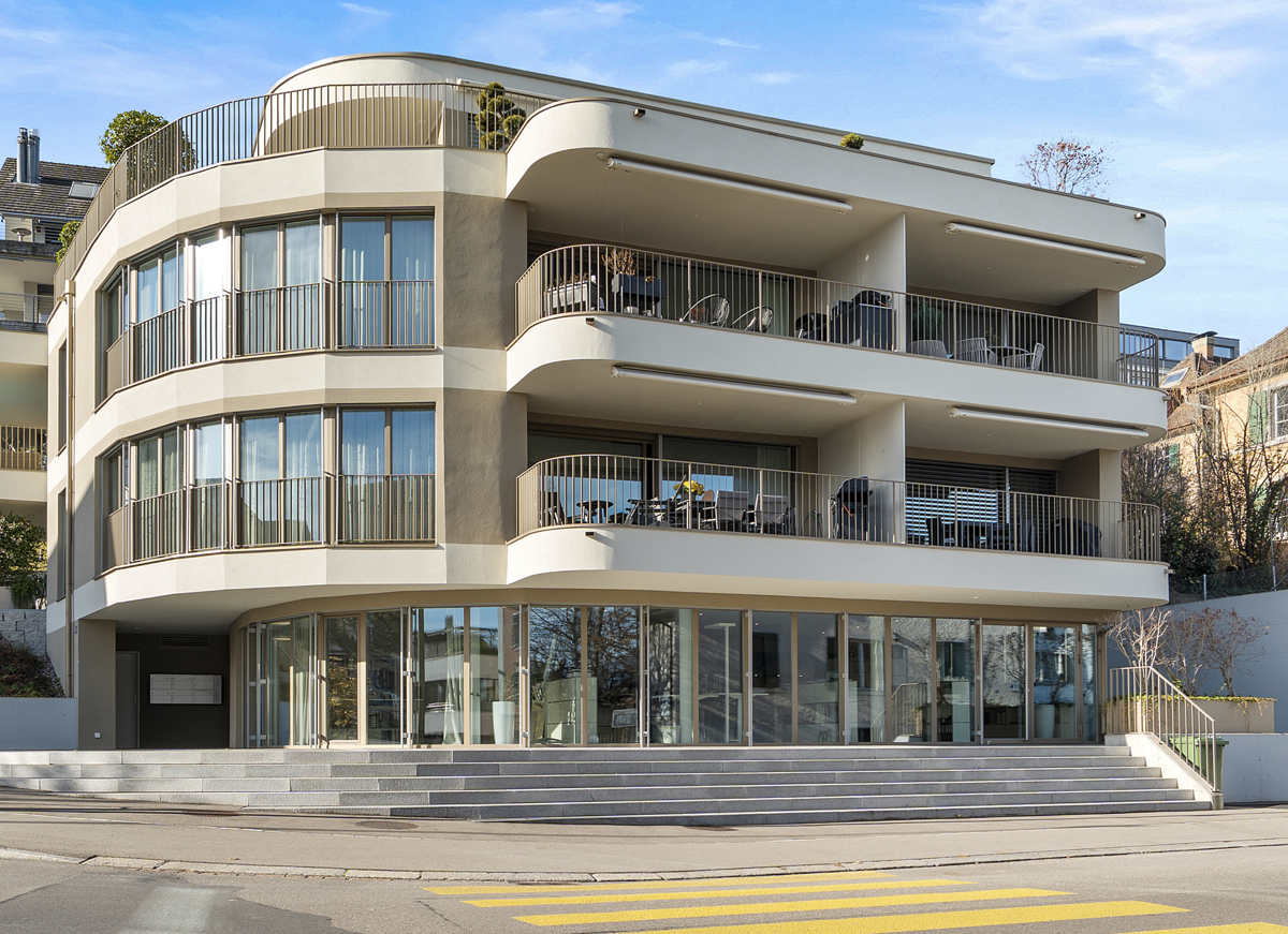 Contemporary multi-storey building with a curved facade, several balconies, glass railings, and a modern glass entrance.