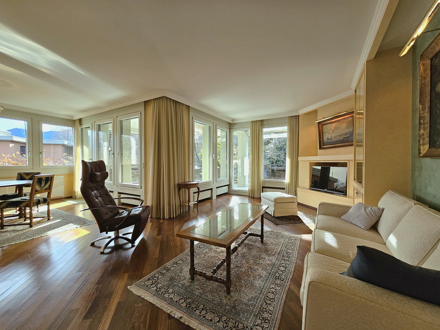 modern living room with hardwood floors, beige couch, fireplace, glass coffee table, large windows, view of mountains