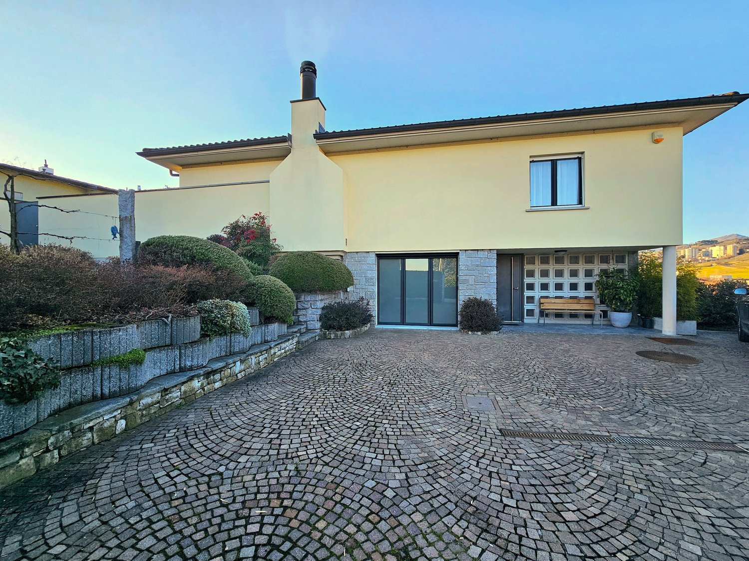 two-story house, yellow exterior, brick and white pillars, large windows, brick driveway