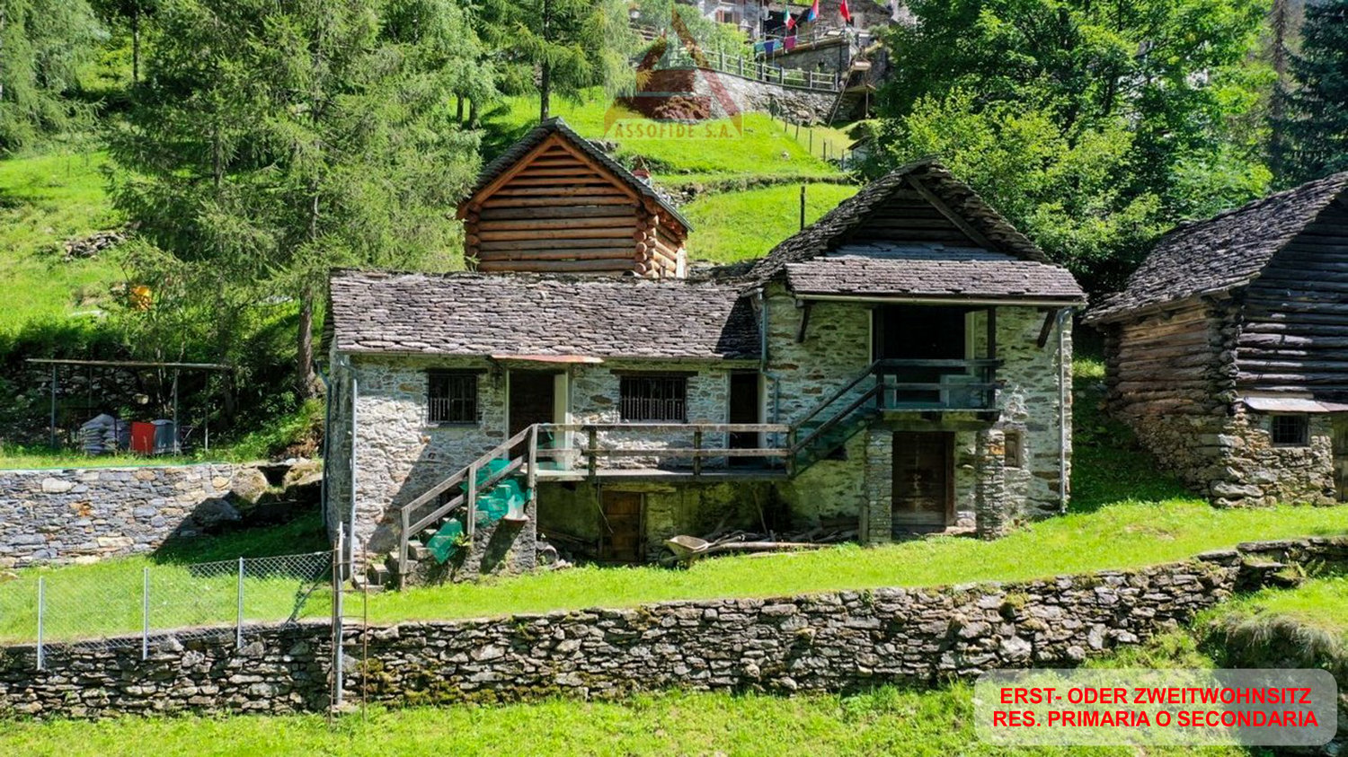 Traditional stone and wooden cabin-style houses in a lush, green mountain setting with a waterfall or stream in the background.