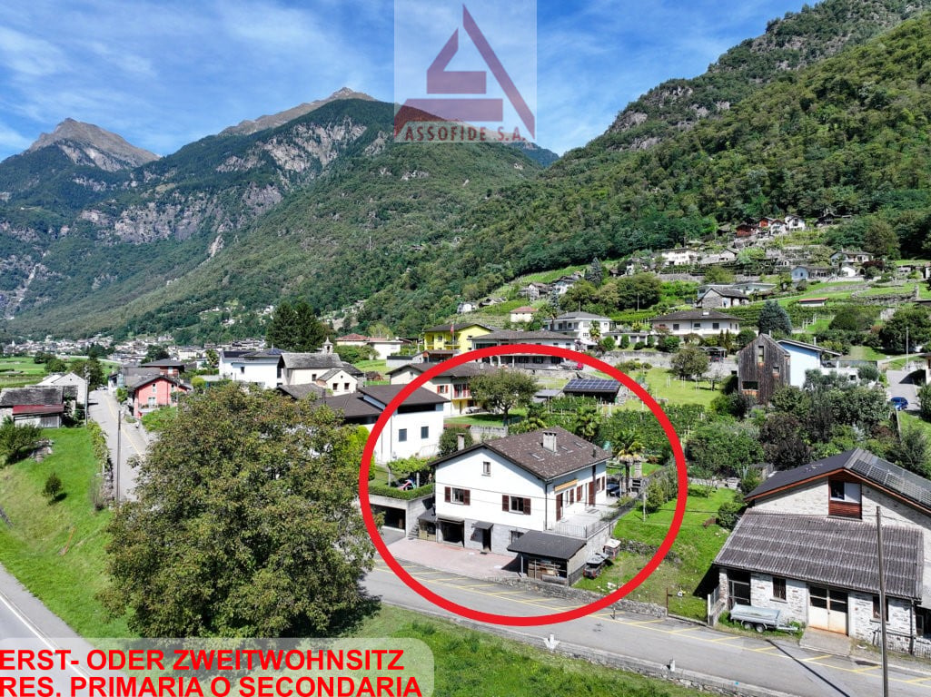 House in mountain village, white exterior, large windows, driveway, surrounding trees and plants