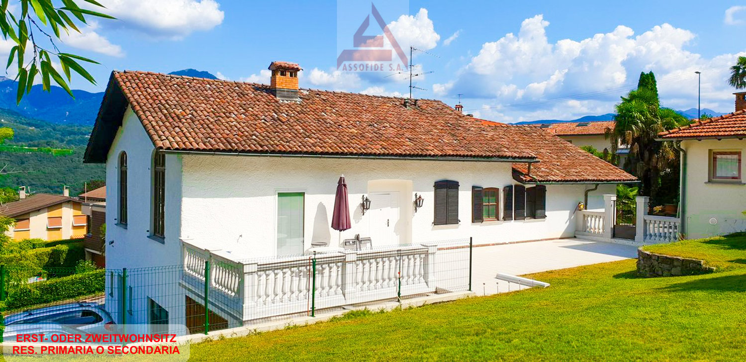 House with brown roof, white exterior, large balcony with railings, small fenced garden