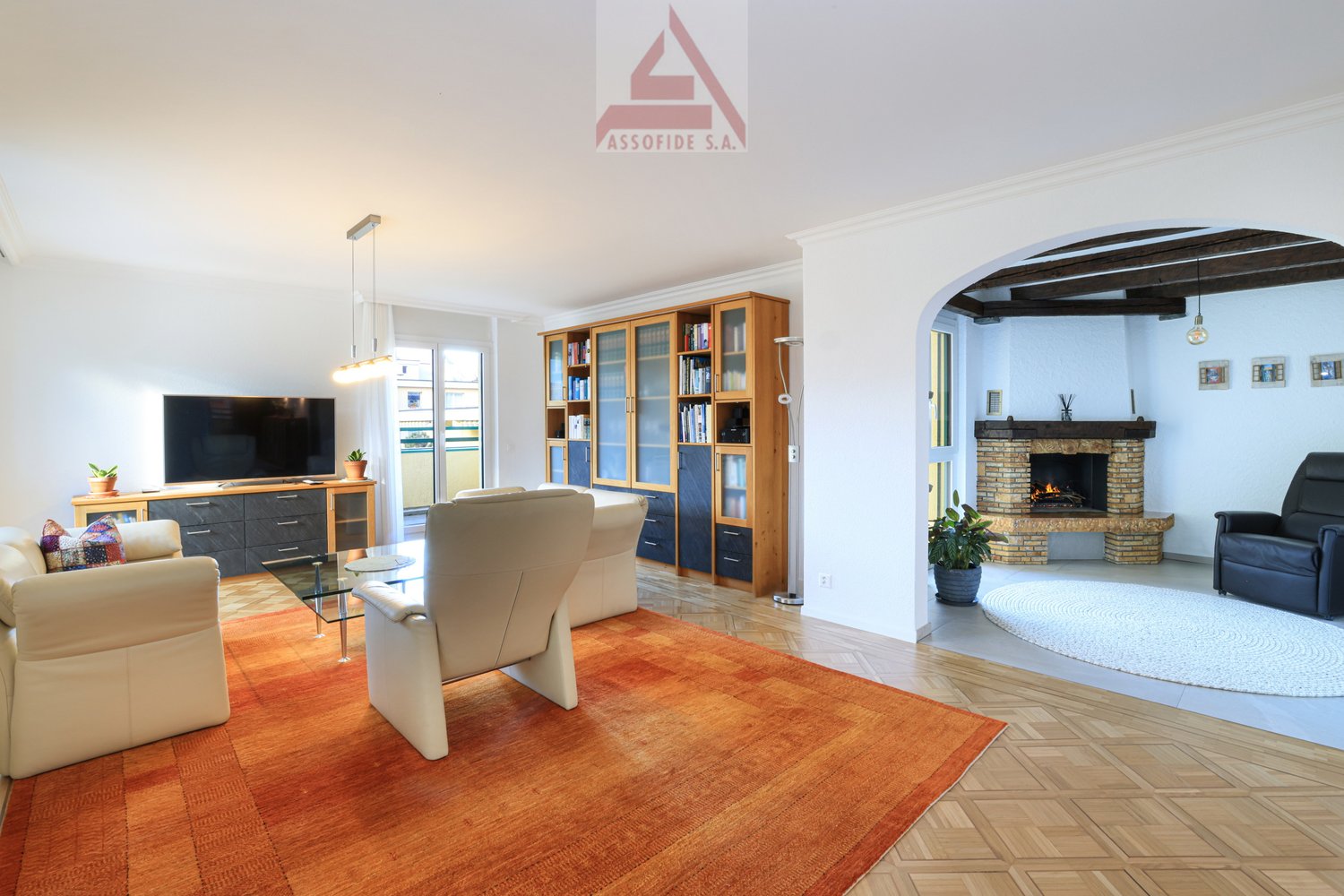 wood floor, white walls, fireplace, tv, entertainment center, bookshelves, white leather couches, armchairs, coffee table, carpet, potted plants