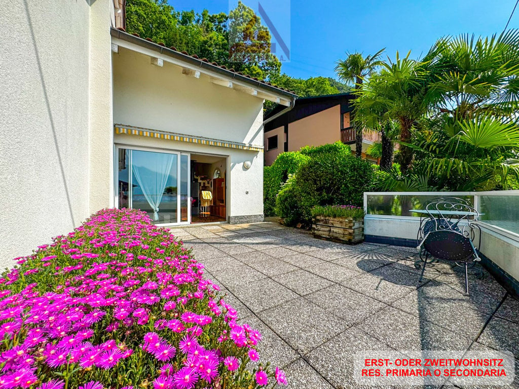 white house, glass door, balcony, patio with flowers, table and chairs, garden, trees