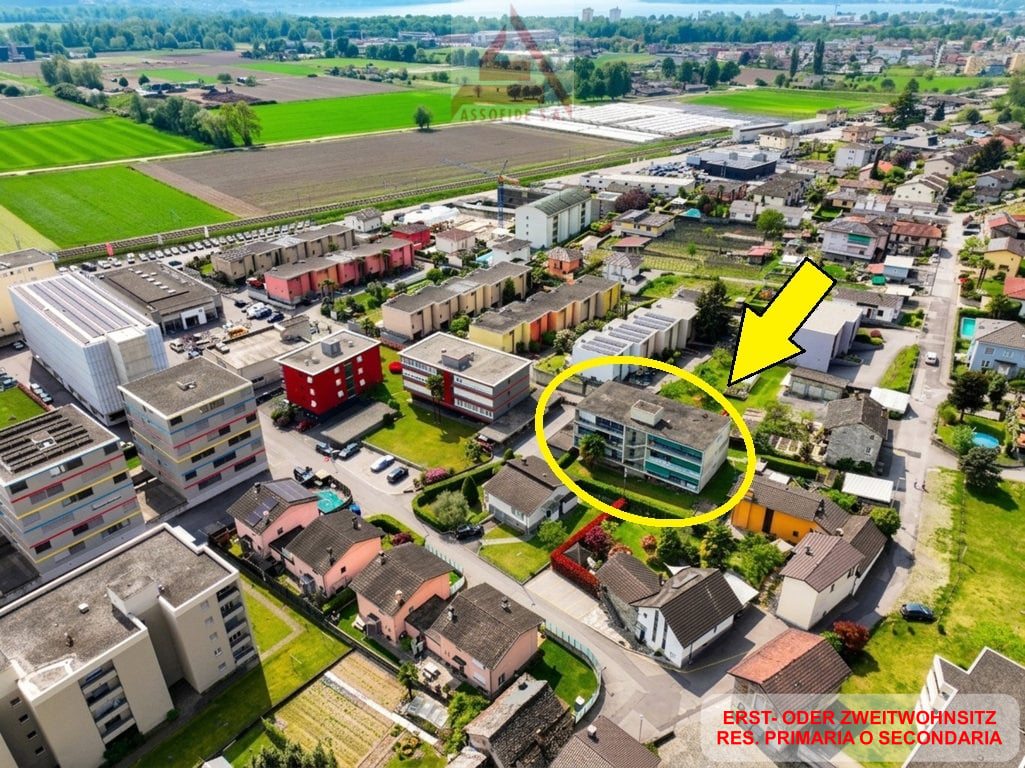 Aerial view of a residential area with various buildings, including a highlighted building with a yellow circle and arrow pointing to it.