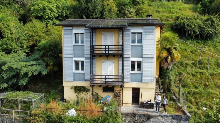 2 story house, yellow and gray exterior, balconies, surrounded by lush greenery