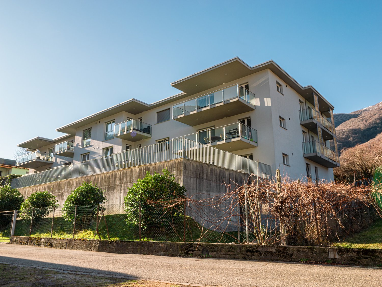 Multi-story apartment building with balconies, located on a hillside with a view of the surrounding mountains and landscape.