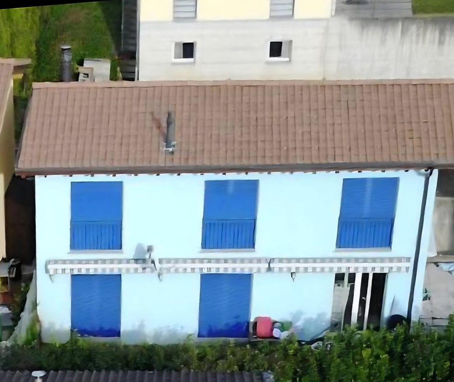 White house with blue shutters, brown roof, raised ground floor, garden