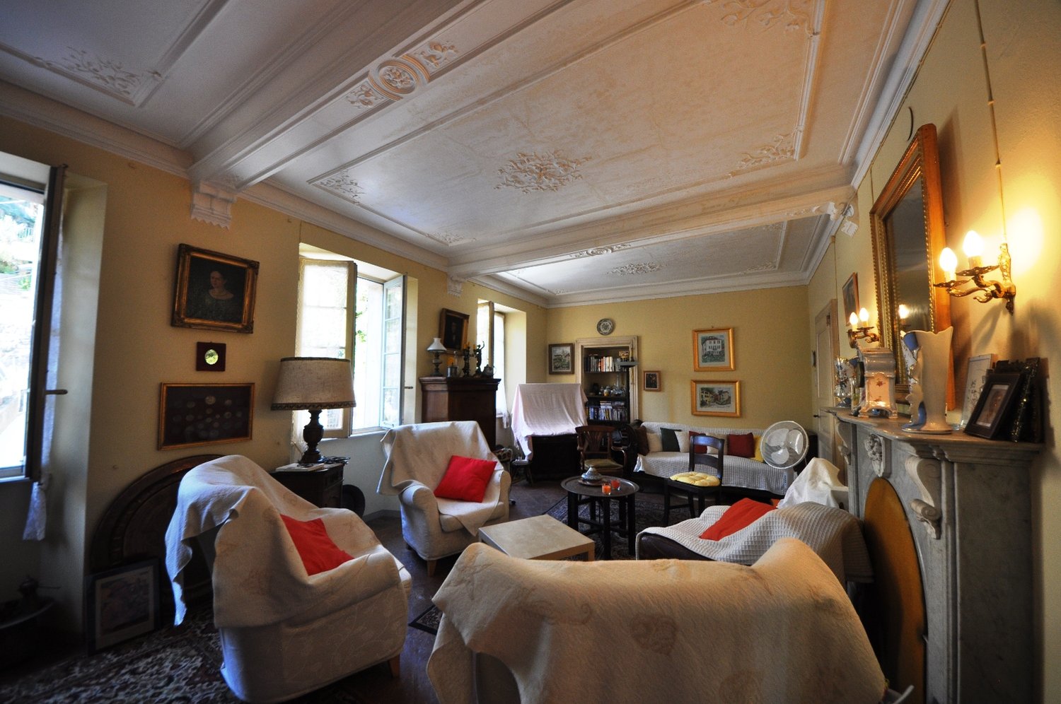 Spacious living room with ornate ceiling, large windows, antique furniture, artwork, and a fireplace