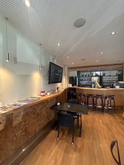 A room with a wooden floor, a counter, a table, chairs, a television, and a refrigerator.