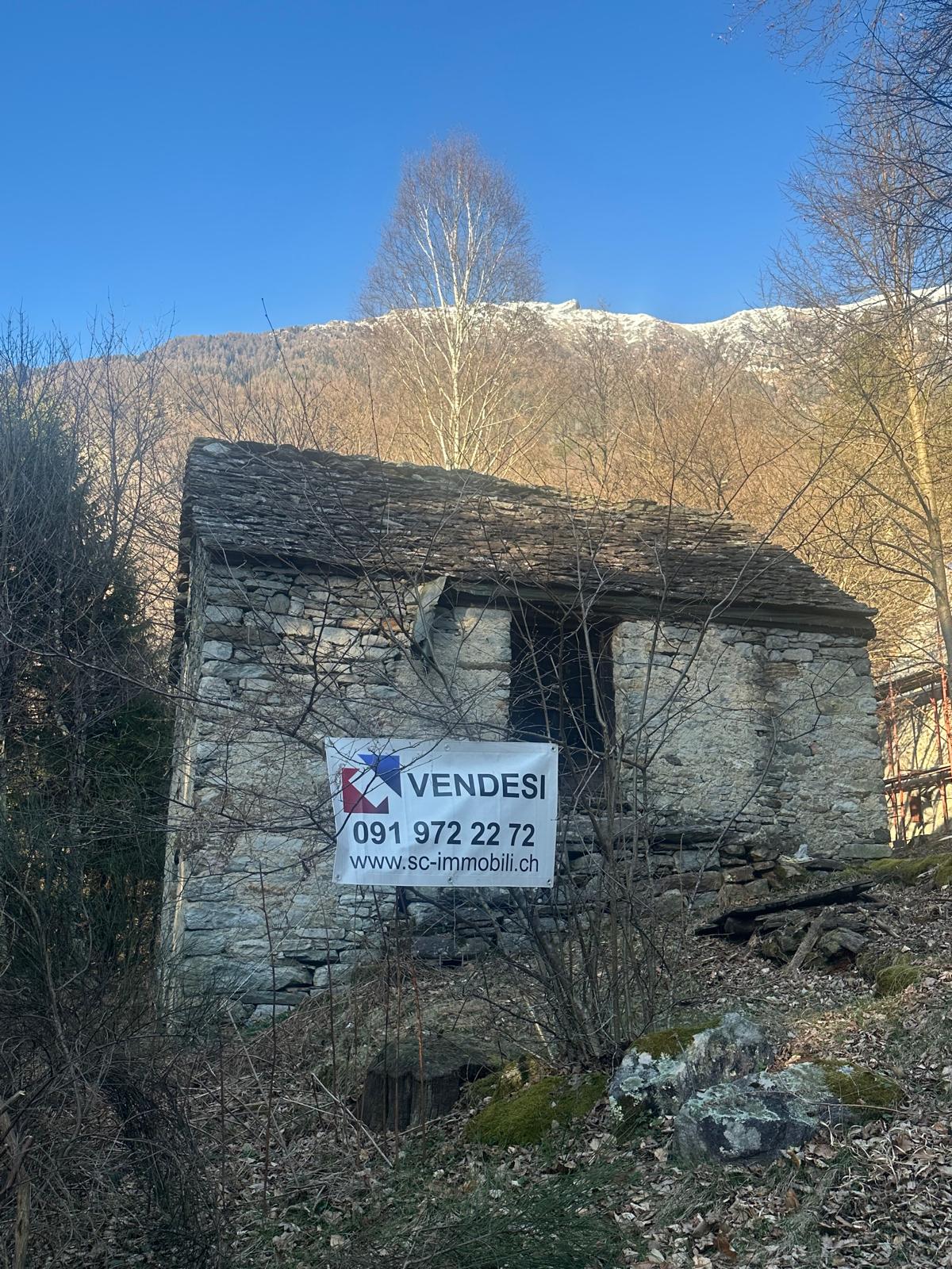 Old stone house, located on a hillside, with a slate roof, surrounded by trees, with a sign indicating it is for sale