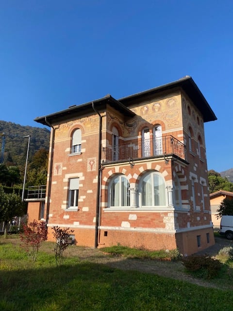 Villa with brick walls, wooden entrance, large arched windows, balcony, lush green surroundings