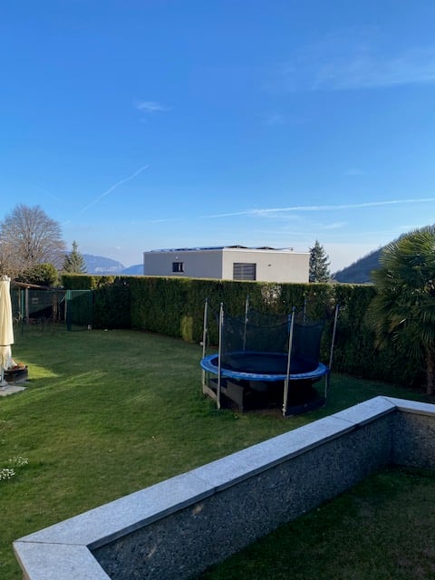 A garden with a trampoline, hedges, and a view of the mountains