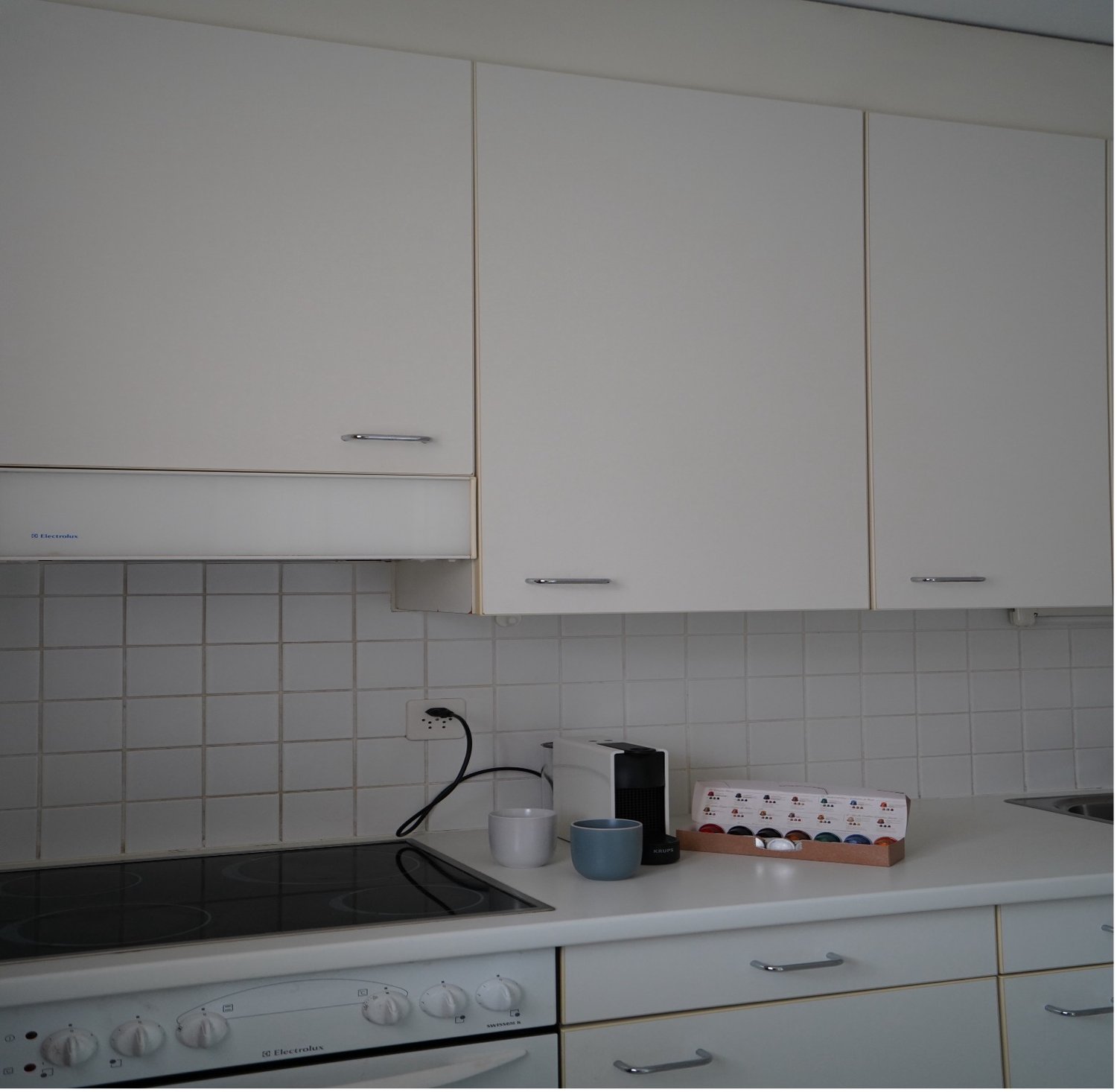 white cabinets, tiled walls, electric stove, coffee maker, coffee cups, small boxes