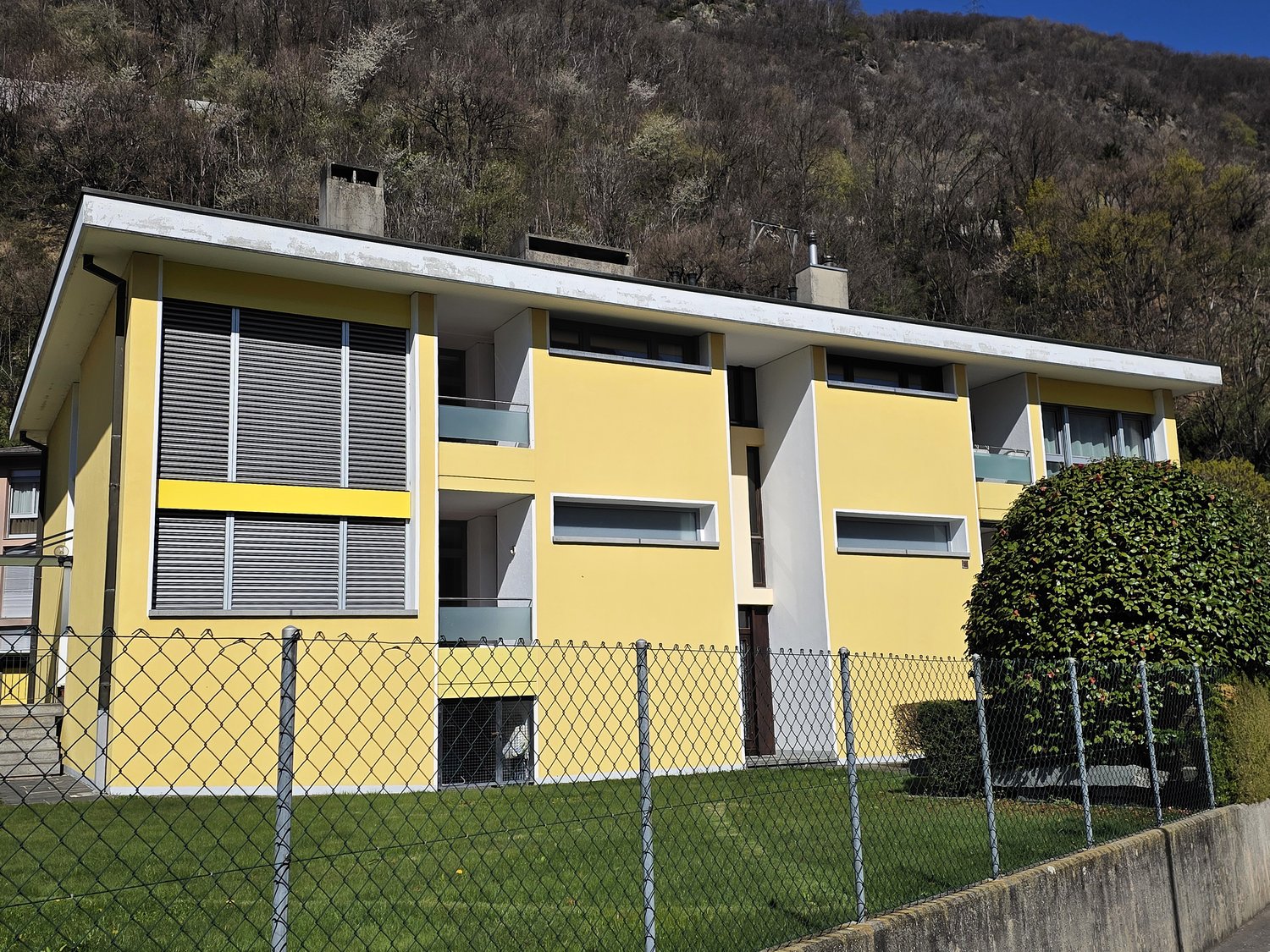 3 story yellow house, white trim, multiple windows, fenced yard, mountain in background
