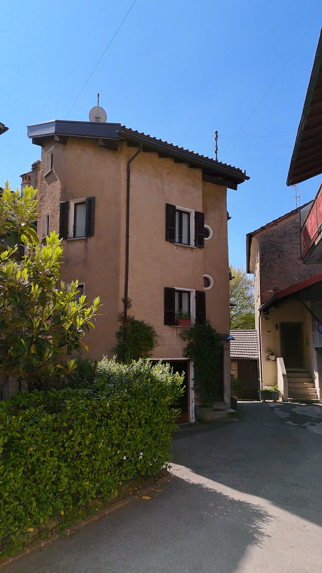 3 story house, beige walls, black shutters, garage, plants, bushes