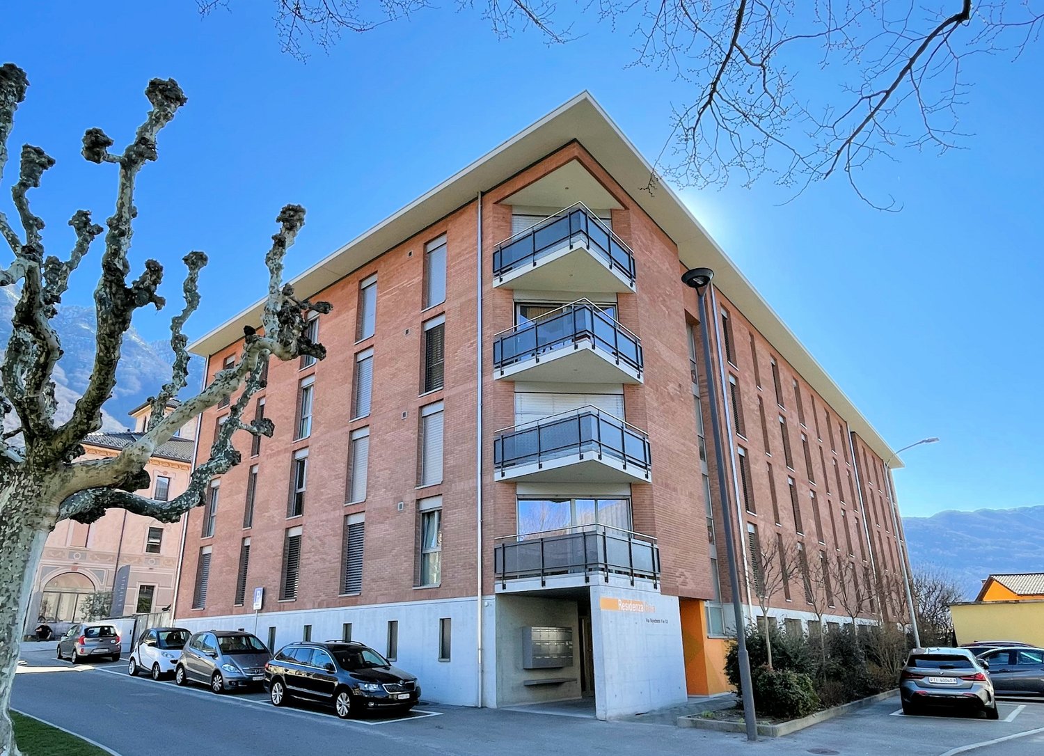 modern apartment building, brick exterior, balconies, street-level garage, several cars parked in front