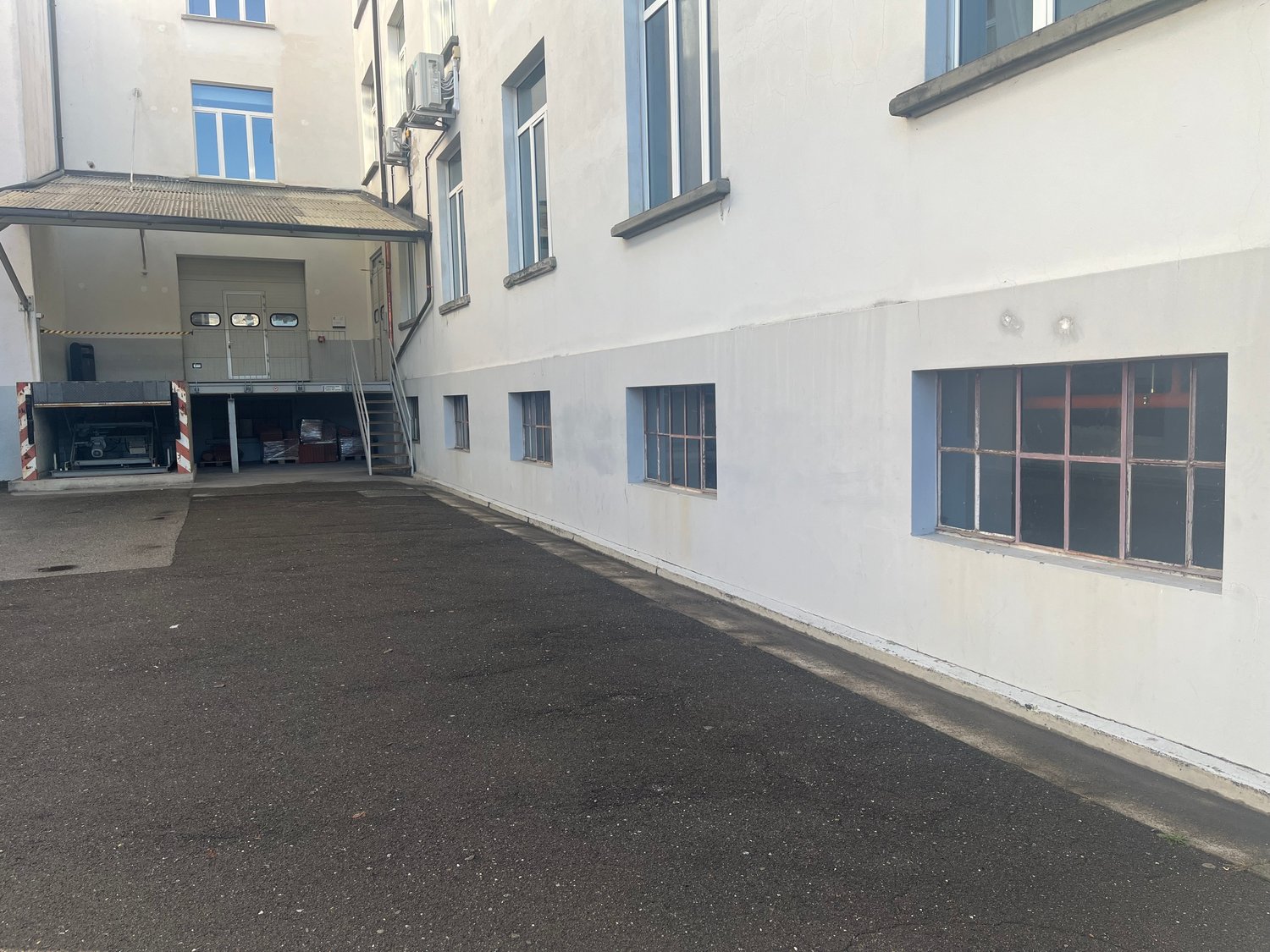 Empty parking lot beside a building, several windows, a garage door, several air conditioning units attached to the wall