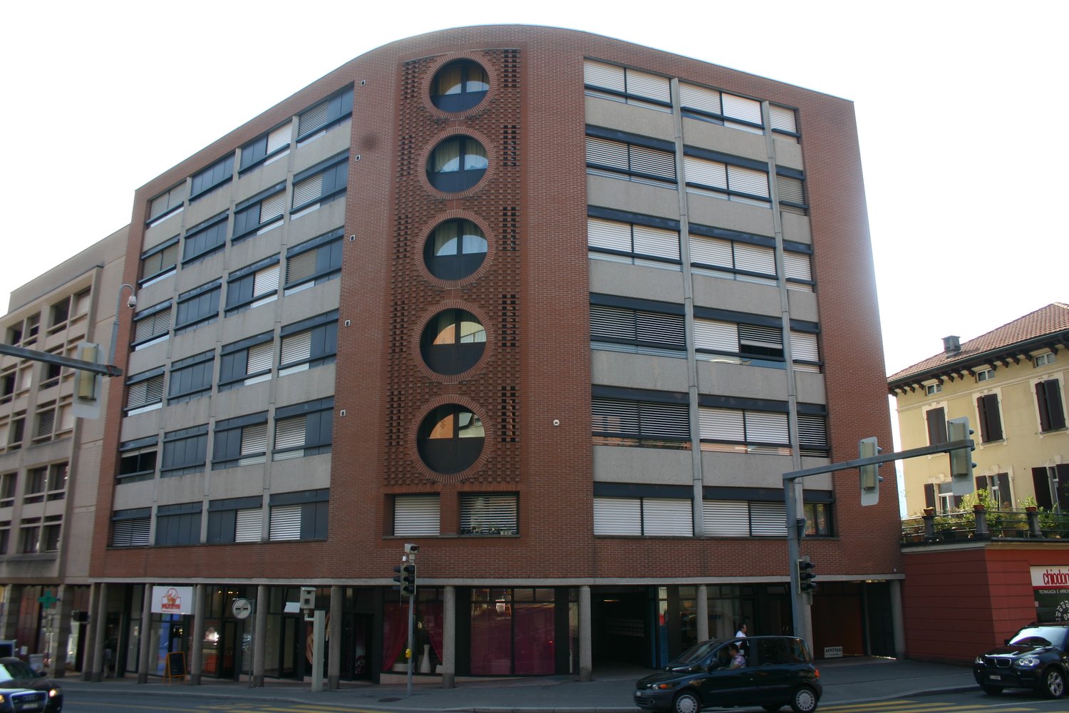 Multi-story brick building with large windows, circular window patterns, and ground-level retail spaces
