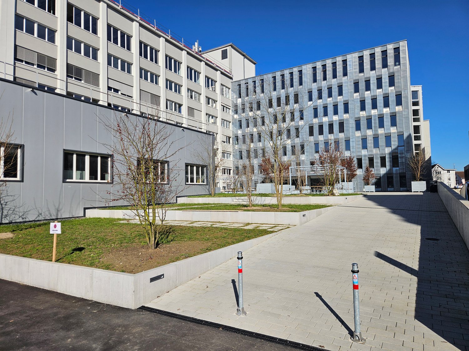 Modern office buildings with glass windows, paved entrance, landscaping, and gray exterior