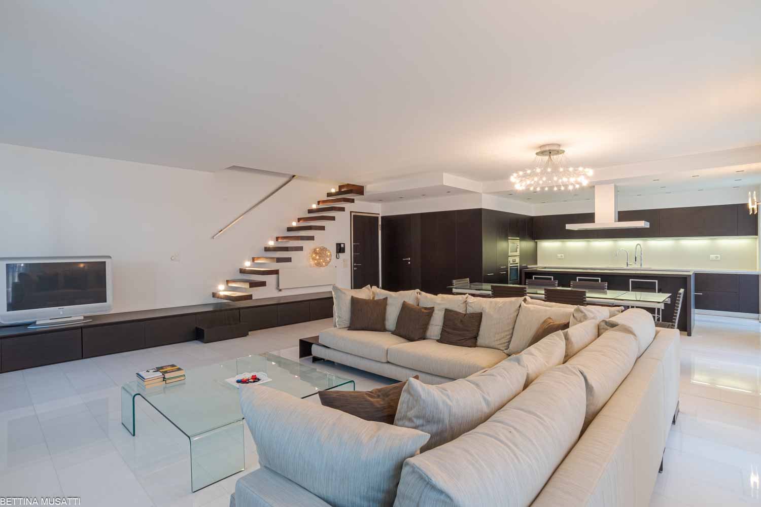 white walls, white floor, large sofa, dining table, television, cabinet with television
