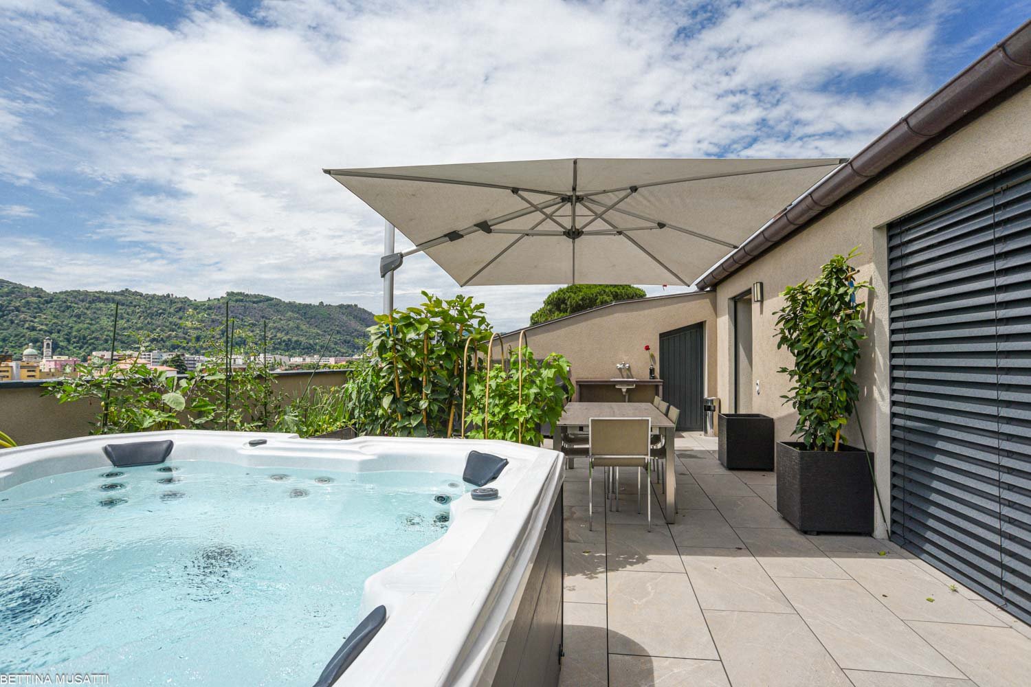 hot tub with umbrella, tiled floor, plants, table, chairs