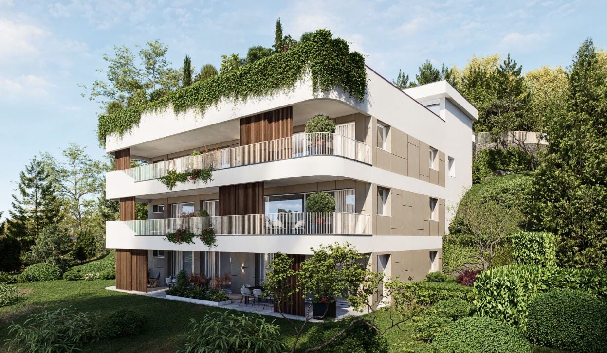 3-story modern apartment building with white exterior, wooden accents, and balconies. The building is surrounded by lush greenery and trees.