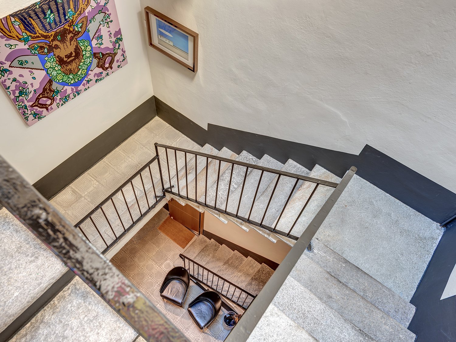 Two-story house, marble floors, staircase, black modern chairs, framed painting on the wall.