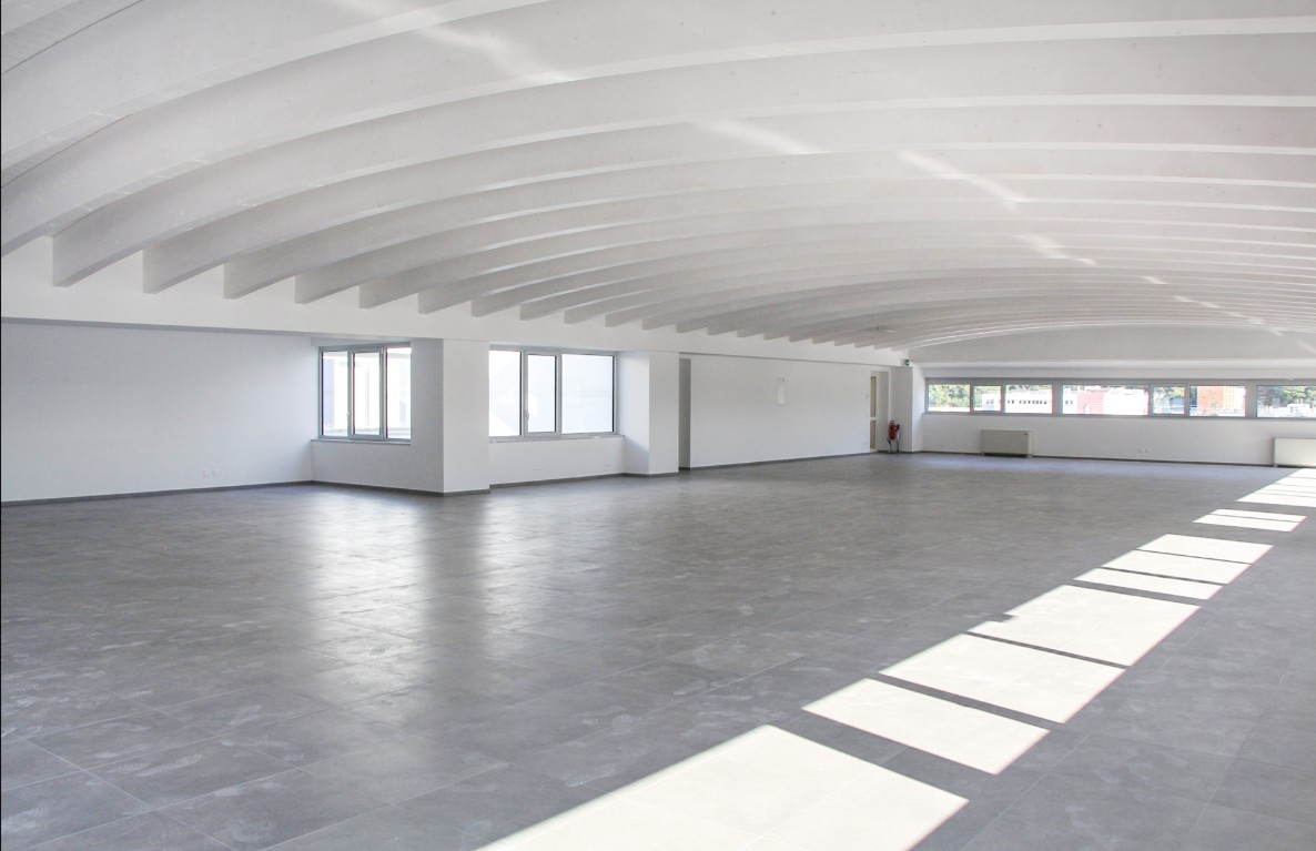 Empty room with high ceilings, grey tiled floor, windows along the walls